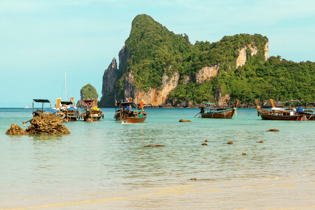 Aerial view of the Phi Phi Islands in Thailand, showing turquoise waters, limestone cliffs, white sandy beaches, and lush tropical greenery.